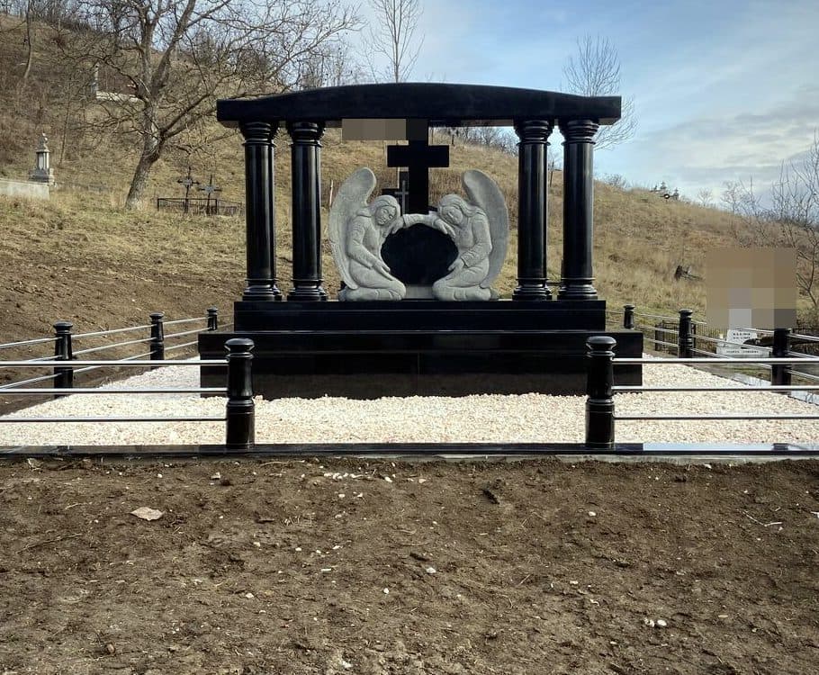 Monument funerar la comandă tip baldachin din granit negru cu îngeri sculptați și cruce, montat în cimitir.