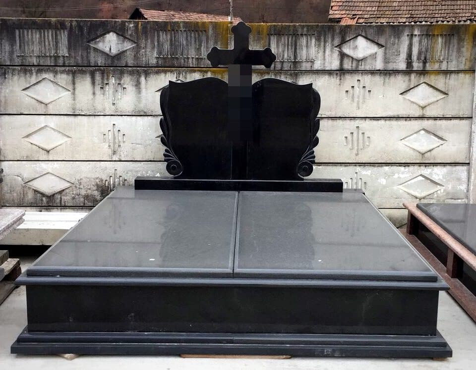 Monument funerar dublu din granit negru cu cruce sculptată, expus în atelierul Mogut.
