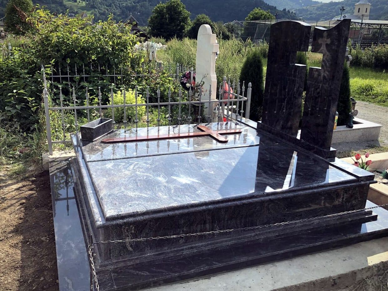 Monument funerar dublu din granit albastru Bahama, montat în cimitir cu priveliște spre munți.