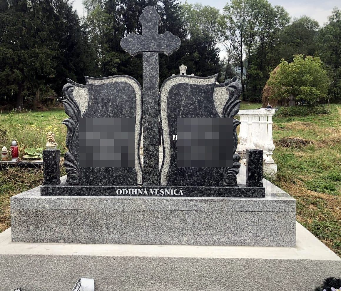 Monument funerar dublu din granit negru cu fulgi, cu cărți sculptate și cruce centrală, montat în cimitir.