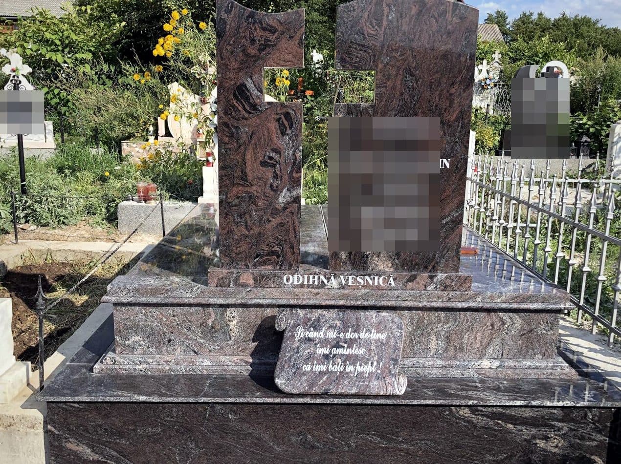 Monument funerar dublu din granit roșu multicolor cu cruce decupată, montat în cimitir.