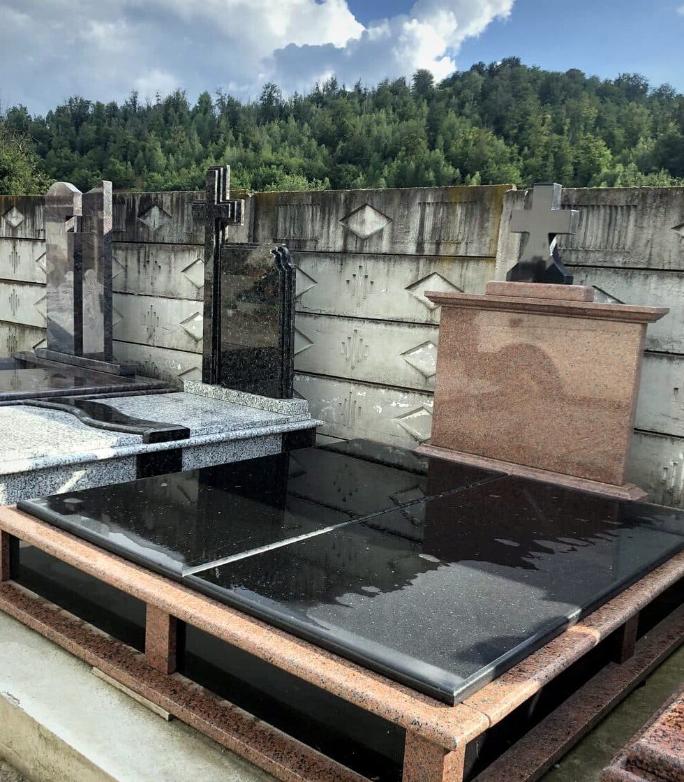 Monument funerar din granit negru cu cadru din granit roșu, montat în cimitir cu priveliște spre pădure.