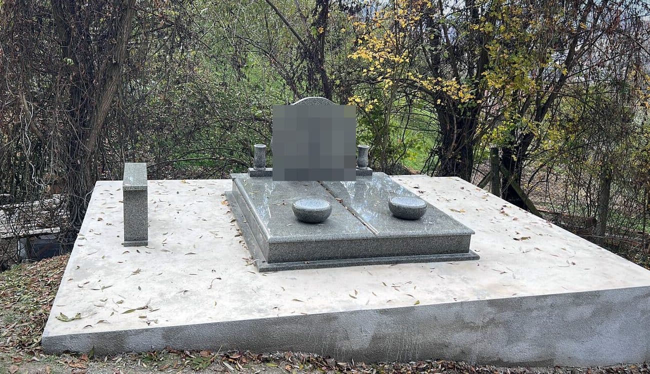 Monument funerar premium din granit gri pe platformă amplă de travertin, montat în cimitir.