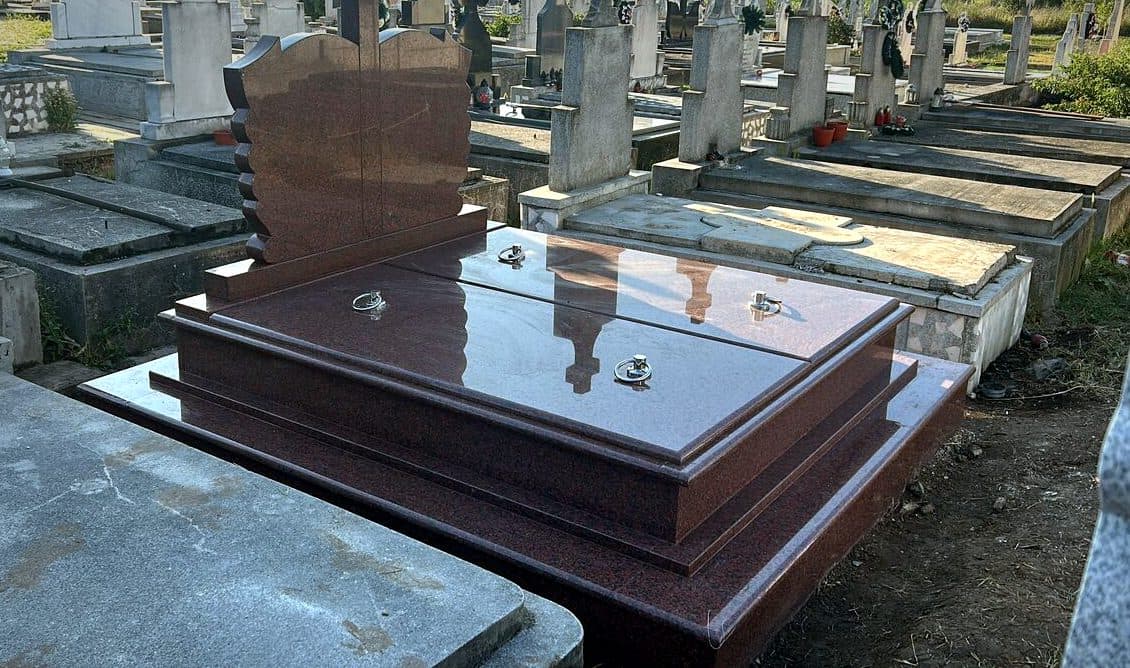 Monument funerar premium din granit roșu cu cruce sculptată, montat în cimitir.