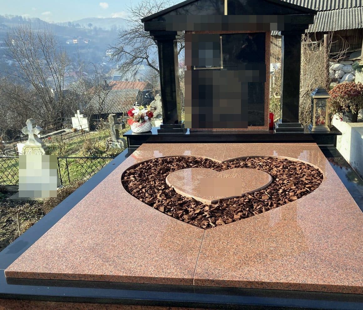 Monument funerar premium din granit roșu cu lespede în formă de inimă și edicul cu cruce, montat în cimitir cu priveliște spre sat.