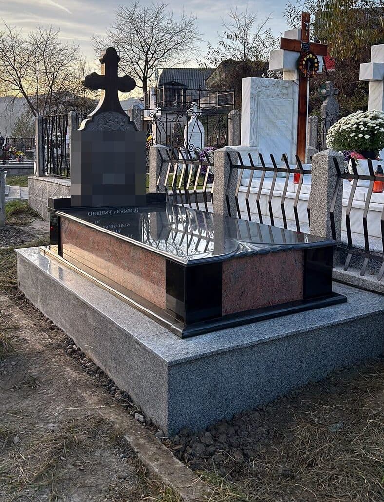 Monument funerar premium din granit roșu și negru cu cruce, montat în cimitir în lumină de seară.