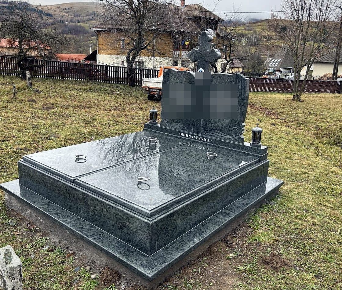 Monument funerar premium din granit verde cu cărți deschise sculptate și cruce, montat în cimitir cu priveliște spre sat.