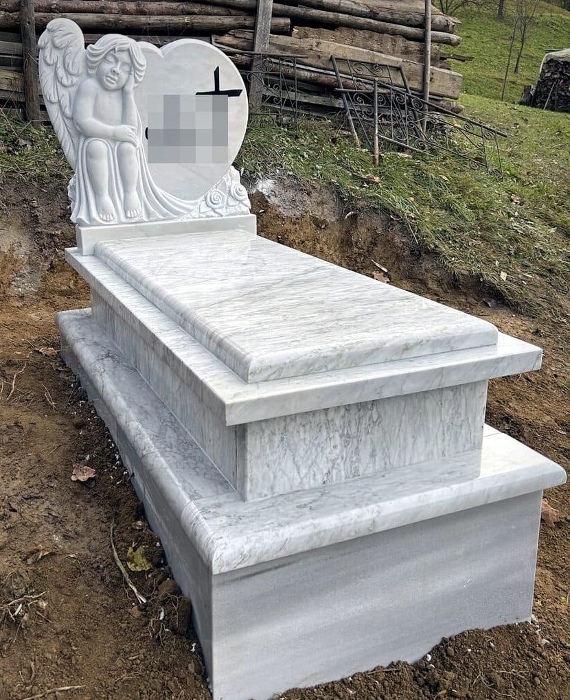 Monument funerar premium din marmură albă cu înger sculptat sprijinit pe o inimă, montat în cimitir.