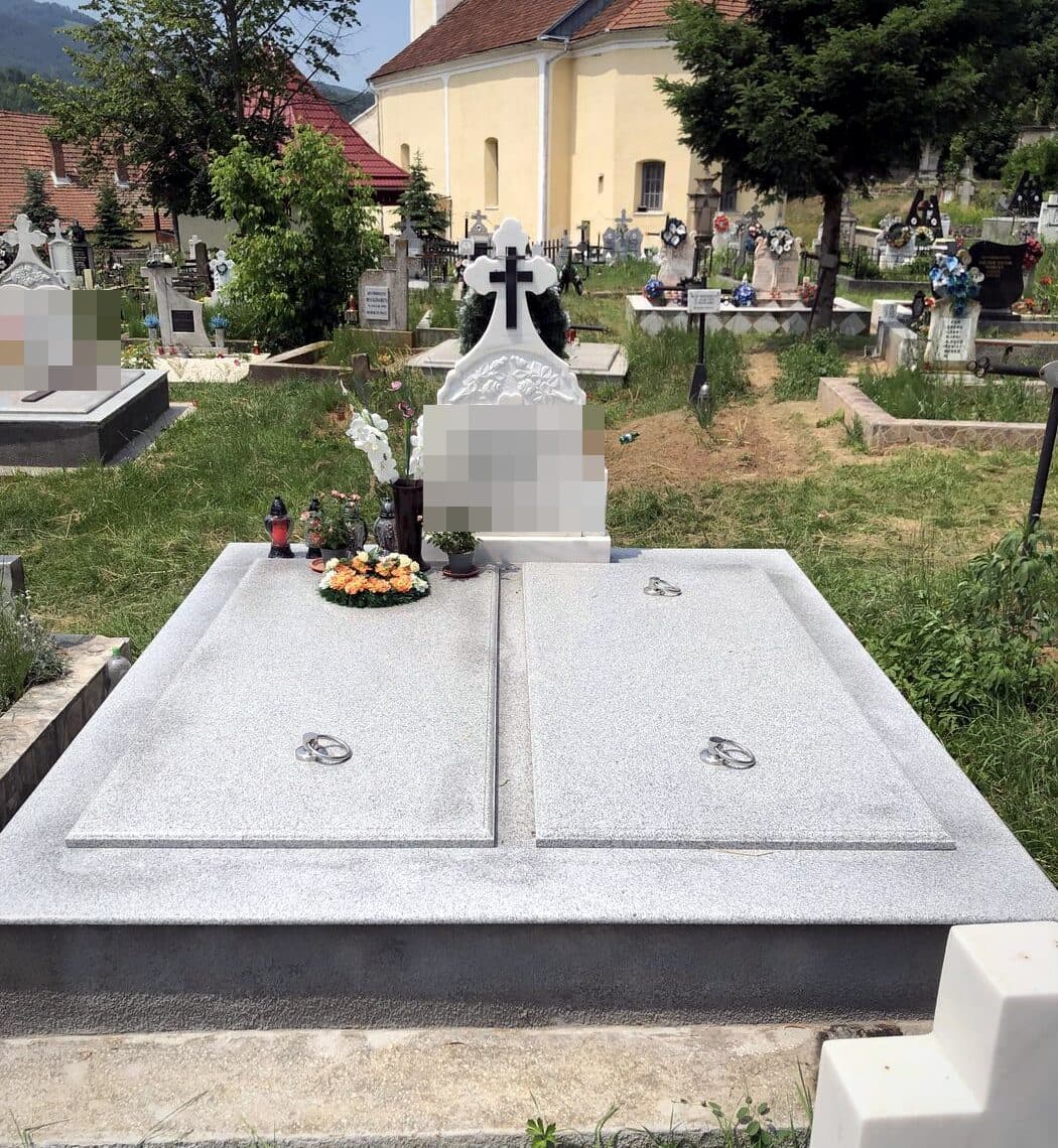 Mormânt clasic dublu din granit gri cu cruce din marmură albă, montat în cimitir lângă biserică.