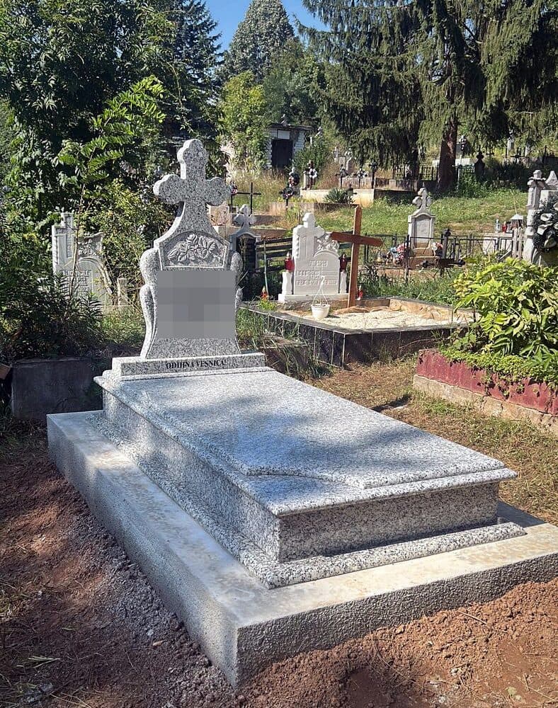 Mormânt clasic din granit gri cu cruce și trandafir sculptat, montat în cimitir.