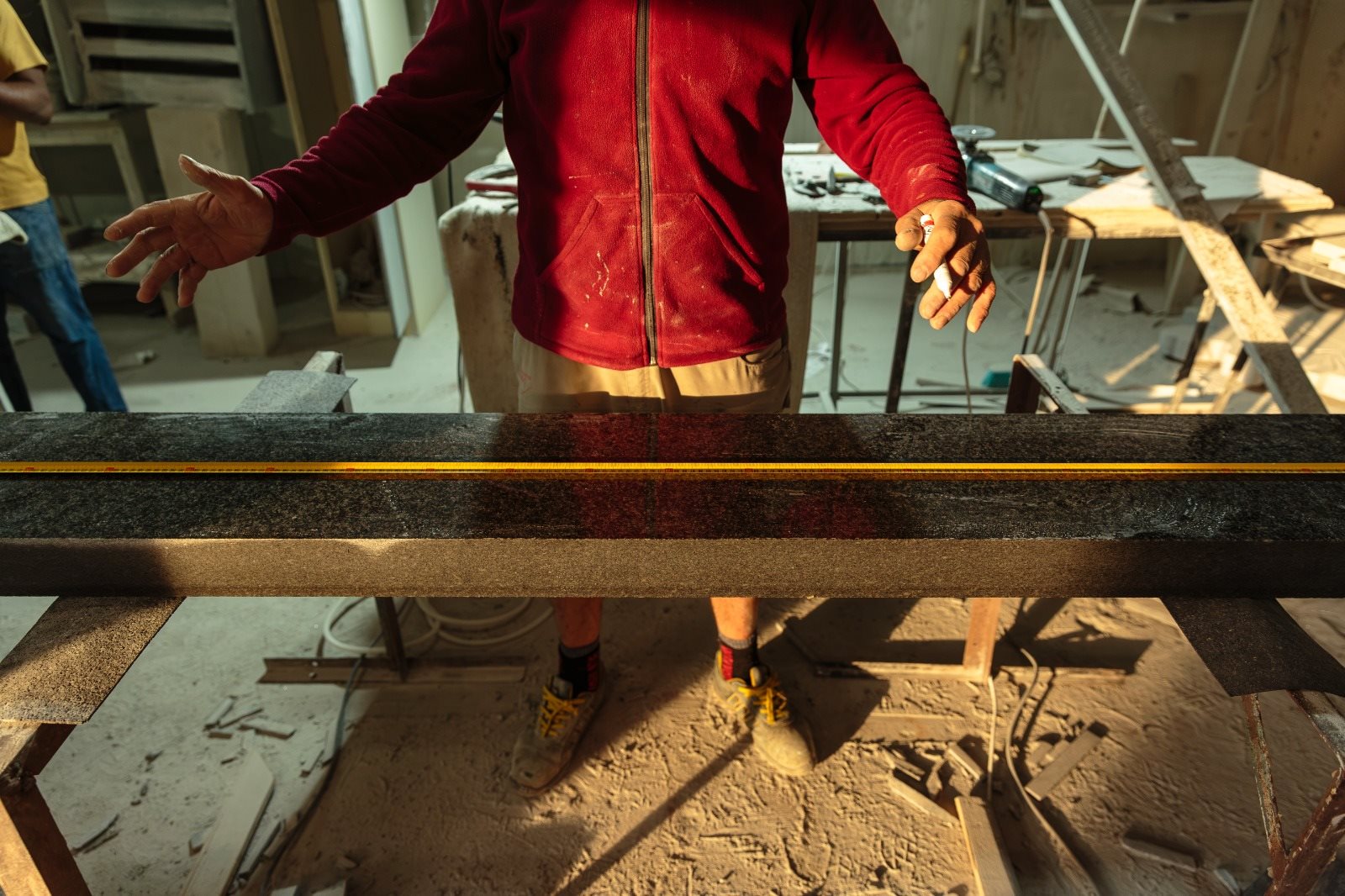 Meșter Mogut măsurând cu ruleta o placă lungă de granit negru lustruit, pe capre, în atelier