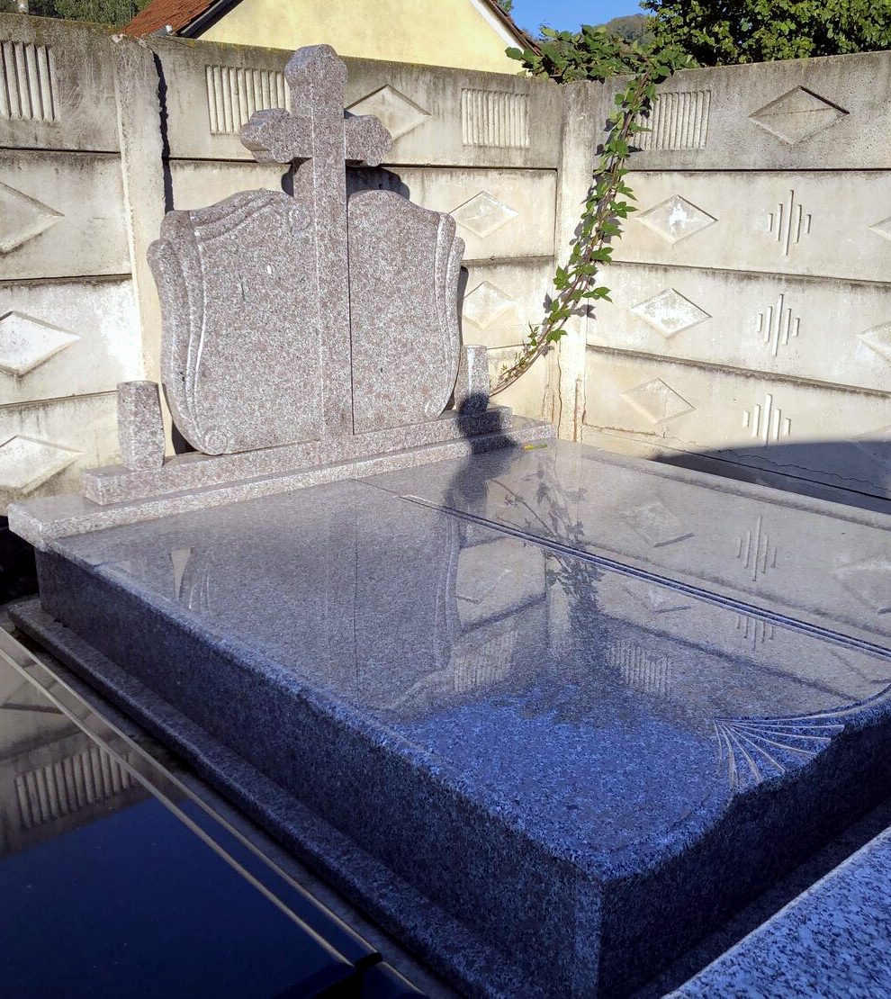 Monument funerar din granit roz cu cruce și capac lustruit, montat în cimitir, fotografiat la predare